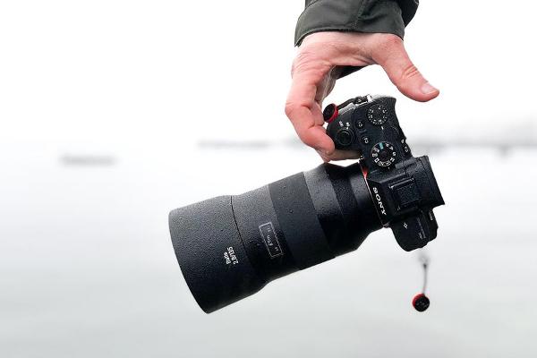 Das Bild zeigt eine Hand, die eine schwarze Kamera mit größerem Objektiv hält.