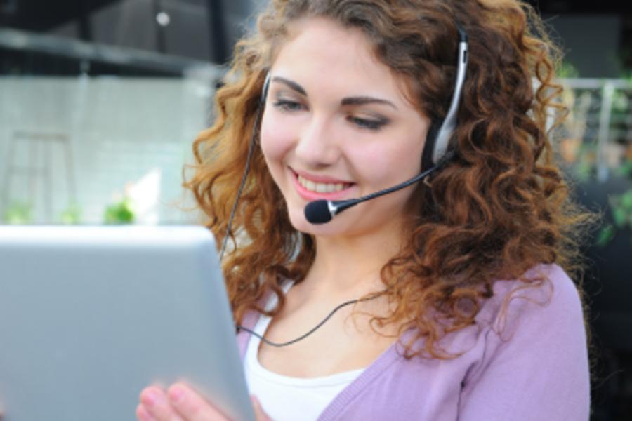 Das Bild zeigt eine junge Frau, die mit Headset vor einem Bildschirm sitzt.  Das Bild zeigt eine junge Frau, die mit Headset vor einem Bildschirm sitzt.