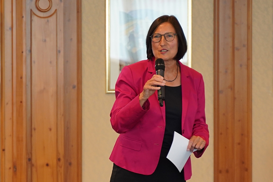 Das Bild zeigt die Vorstandsvorsitzende Helga Schwitzer. Sie trägt einen pinken Blazer und hält ein Mikrofon in der einen Hand. In der anderen Hand hält sie ein Blatt Papier.   Das Bild zeigt die Vorstandsvorsitzende Helga Schwitzer. Sie trägt einen pinken Blazer und hält ein Mikrofon in der einen Hand. In der anderen Hand hält sie ein Blatt Papier.