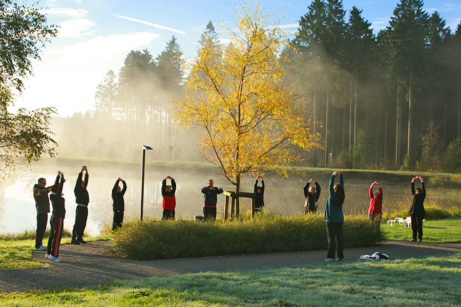 Erwachsene stehen im Sonnenschein am See und praktizieren Atemübungen Erwachsene stehen im Sonnenschein am See und praktizieren Atemübungen