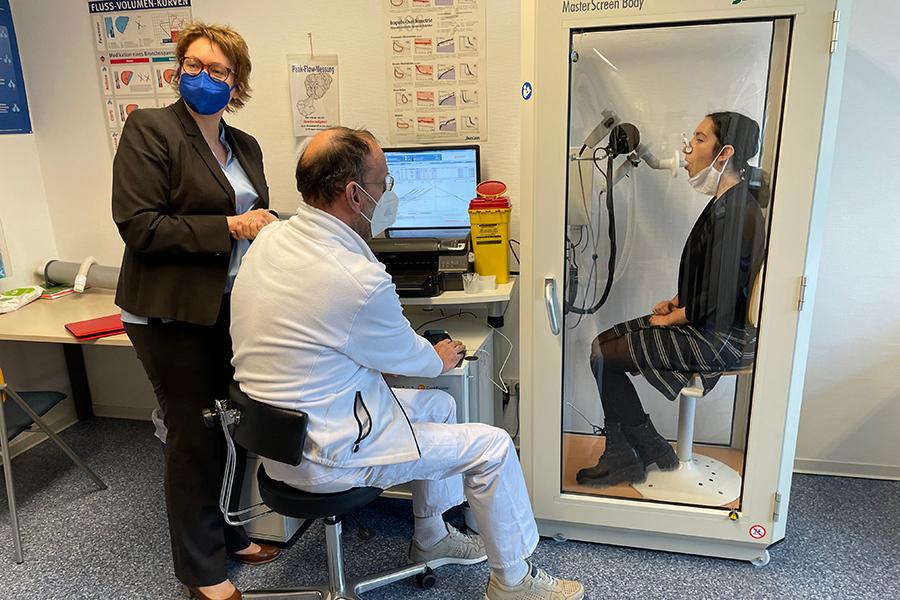 Die niedersächsische Gesundheitsministerin Daniela Behrens steht bei einem am Tisch sitzenden Therapeuten, der gerade einen Lungenfunktionstest durchführt. Die niedersächsische Gesundheitsministerin Daniela Behrens steht bei einem am Tisch sitzenden Therapeuten, der gerade einen Lungenfunktionstest durchführt.