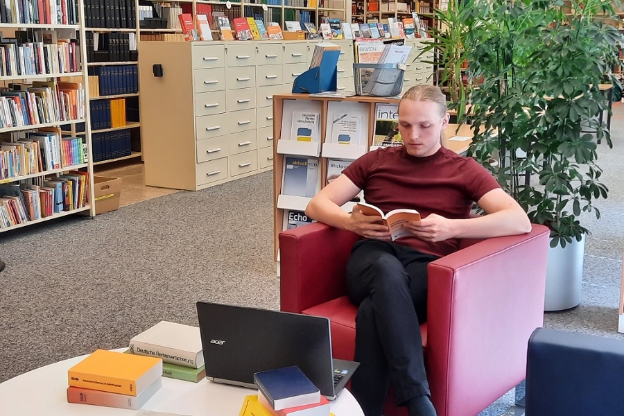 Lesesaal mit Sitzecke und Einblick in die Räumlichkeiten. Im Vordergrund sitzt ein lesender Bibliotheksgast Lesesaal mit Sitzecke und Einblick in die Räumlichkeiten. Im Vordergrund sitzt ein lesender Bibliotheksgast