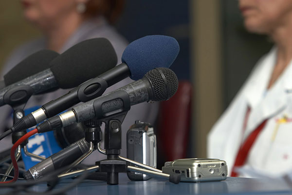 Viele Mikrofone stehen auf dem Tisch vor einer Rednerin