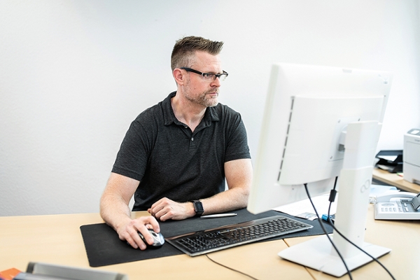 Ein Mann sitzt an einem Schreibtisch und arbeitet an einem Computer (verweist auf: Arbeitgeber im Blick: Die Betriebsprüfung)