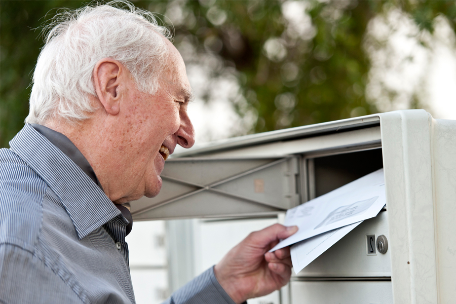 Ein älterer Mann holt lächelnd die Post aus dem Briefkasten. Ein älterer Mann holt lächelnd die Post aus dem Briefkasten.