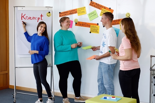 Eine Gruppe lächelnder junger Leuten arbeitet zusammen an einem Whiteboard