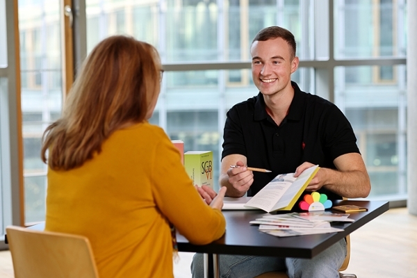 Ein freundlich lächelnder junger Mann berät eine Kundin zu Rentenfragen. Ein freundlich lächelnder junger Mann berät eine Kundin zu Rentenfragen.