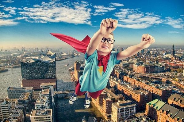 Ein Junge mit rotem Cape fliegt in Superhelden-Pose über die Hamburger Hafencity mit der Elphi. Ein Junge mit rotem Cape fliegt in Superhelden-Pose über die Hamburger Hafencity mit der Elphi.