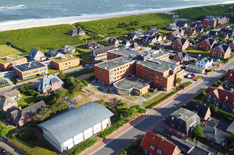 Die Fachklinik Sylt für Kinder und Jugendliche von oben. Im Hintergrund sieht man das Meer.