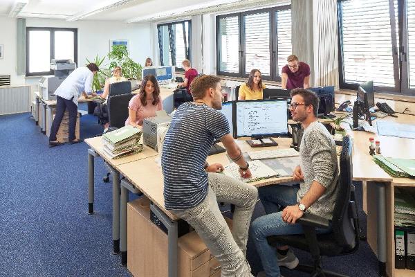 Foto: Nachwuchskräfte bei ihrer praktischen Ausbildung in einem Großraumbüro.