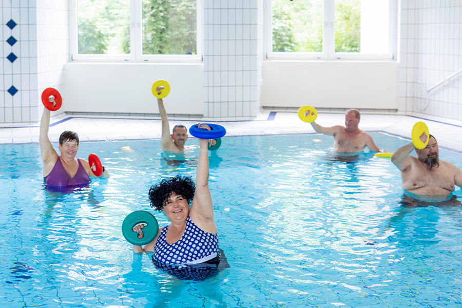 Mehrere Patienten trainieren bei der Wassergymnastik mit Gewichten. Mehrere Patienten trainieren bei der Wassergymnastik mit Gewichten.