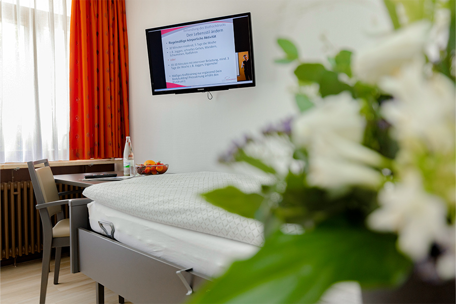 Ein beispielhaftes Patientenzimmer mit Bett, Sitzecke und Fernseher. Ein beispielhaftes Patientenzimmer mit Bett, Sitzecke und Fernseher.