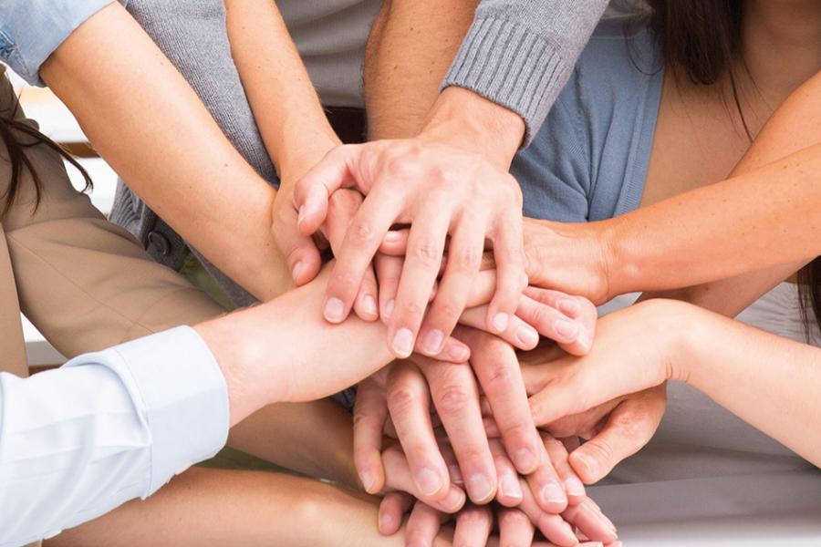 Im Bild sind übereinandergelegte Hände von verschiedenen Personen zu sehen.