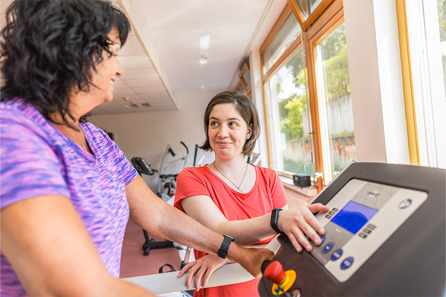 Eine Therapeutin unterstützt eine Patientin beim Training auf dem Laufband. Eine Therapeutin unterstützt eine Patientin beim Training auf dem Laufband.
