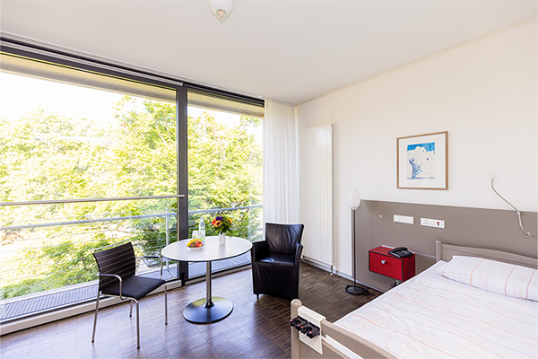 Ein beispielhaftes Patientenzimmer mit Bett, Sitzecke und Balkon. Ein beispielhaftes Patientenzimmer mit Bett, Sitzecke und Balkon.