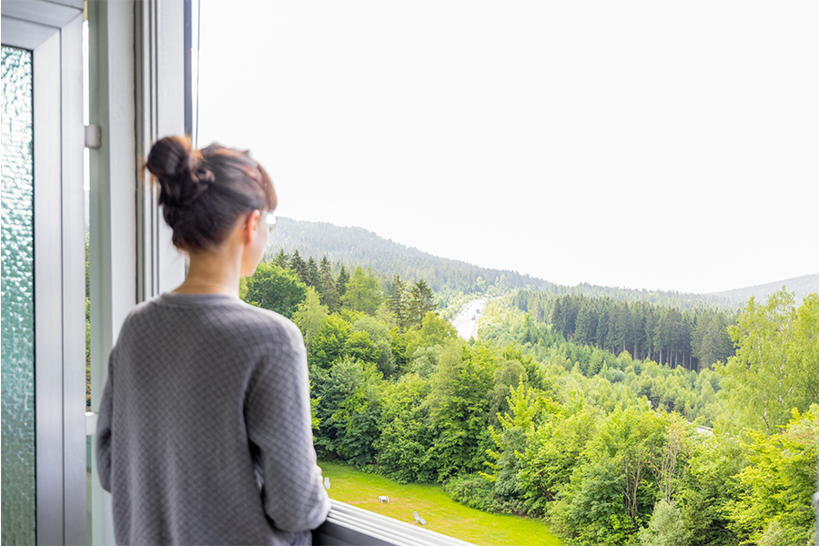 Rückansicht einer Frau, die aus einem Fenster auf einen Wald schaut. Rückansicht einer Frau, die aus einem Fenster auf einen Wald schaut.