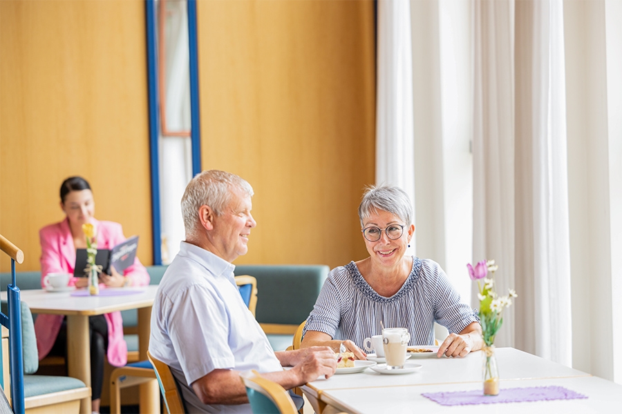 Zwei Personen sitzen an einem Tisch und trinken Kaffee. Im Hintergrund liest eine Frau ein Buch. Zwei Personen sitzen an einem Tisch und trinken Kaffee. Im Hintergrund liest eine Frau ein Buch.