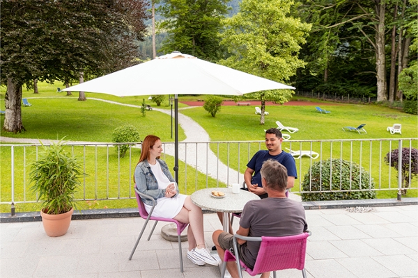 Zwei Männer und eine Frau sitzen um einen Tisch auf der Terrasse der Klinik. Zwei Männer und eine Frau sitzen um einen Tisch auf der Terrasse der Klinik.