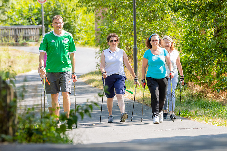 Mehrere Personen beim Nordic Walking durch einen Park. Mehrere Personen beim Nordic Walking durch einen Park.