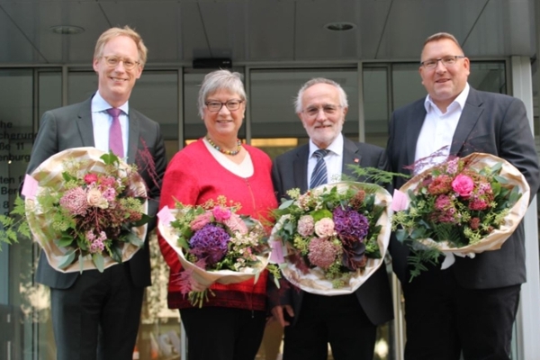 Drei Männer und eine Frau stehen mit Blumensträußen vor dem Haupteingang der DRV Oldenburg-Bremen Drei Männer und eine Frau stehen mit Blumensträußen vor dem Haupteingang der DRV Oldenburg-Bremen