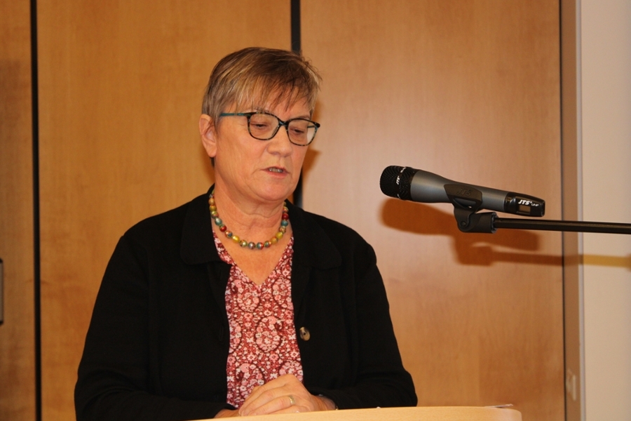 Eine Frau mit Kurzhaarschnitt und Brille hält einen Vortrag am Mikrofon. Eine Frau mit Kurzhaarschnitt und Brille hält einen Vortrag am Mikrofon.