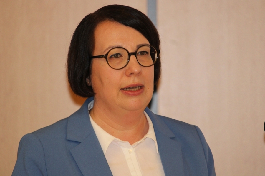 Eine Frau mit Kurzhaarschnitt und Brille hält einen Vortrag am Mikrofon. Eine Frau mit Kurzhaarschnitt und Brille hält einen Vortrag am Mikrofon.