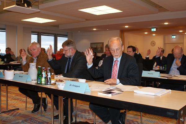 Mehrere Leute sitzen in einer Reihe am Tisch und heben die Hände zur Abstimmung Mehrere Leute sitzen in einer Reihe am Tisch und heben die Hände zur Abstimmung
