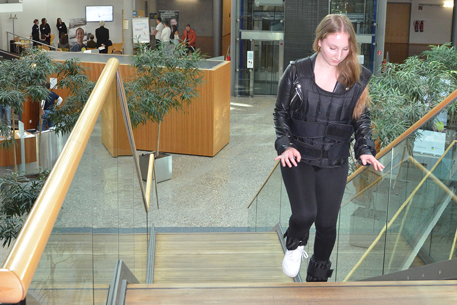 Das Bild zeigt eine Schülerin, die mit einem Altersimmulationsanzug Treppen steigt.