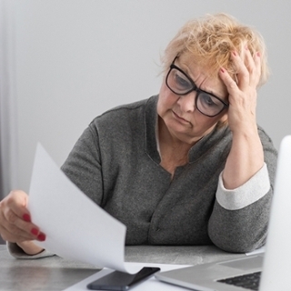 Eine Frau schaut sich eine Rechnung an. Neben ihr steht ein Notebook. Eine Frau schaut sich eine Rechnung an. Neben ihr steht ein Notebook.