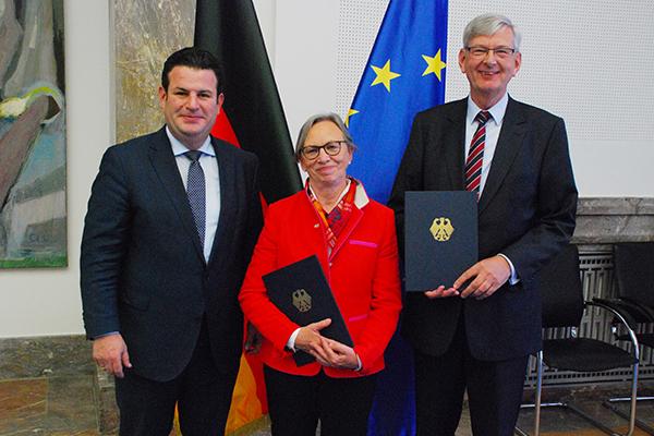 Zwei Männer und eine Frau sind auf dem Bild zu sehen. Die in der Mitte stehende Frau und der rechts stehende Mann halten eine Urkunde in der Hand. Zwei Männer und eine Frau sind auf dem Bild zu sehen. Die in der Mitte stehende Frau und der rechts stehende Mann halten eine Urkunde in der Hand.