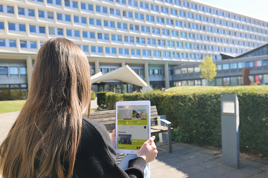 Frau sitzt mit Tablet vor einem Gebäude.