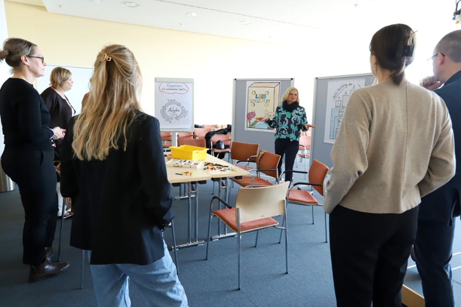 Menschen stehen in einem Raum, eine Frau hält einen Vortrag. Menschen stehen in einem Raum, eine Frau hält einen Vortrag.