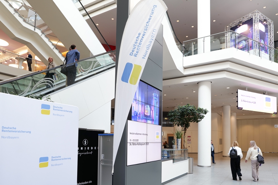 Eine große Halle mit Rolltreppe und Plakaten zum Reha-Kolloquium. Eine große Halle mit Rolltreppe und Plakaten zum Reha-Kolloquium.