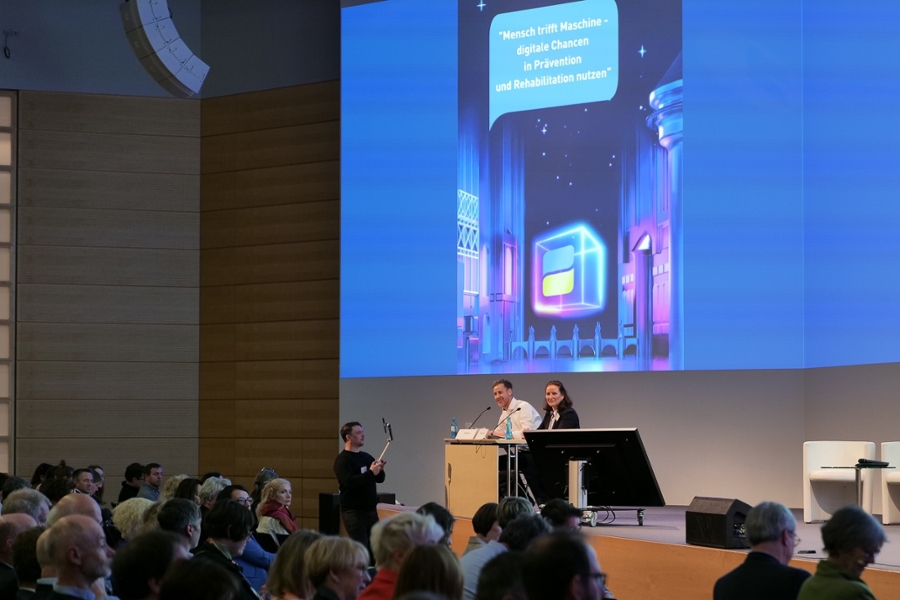 Zwei Menschen sitzen auf der Bühne hinter einem Tisch. Zwei Menschen sitzen auf der Bühne hinter einem Tisch.