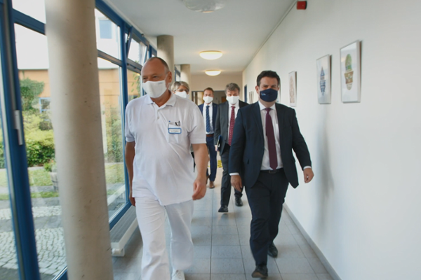 Screenshot aus dem Video: Hubertus Heil und Gundula Roßbach durchqueren begleitet von Klinikpersonal einen Flur