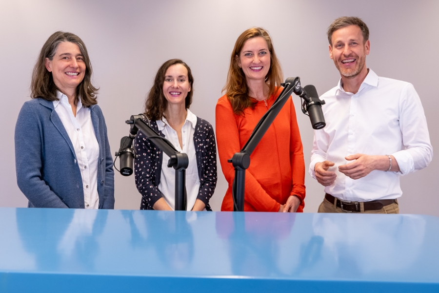 Drei Frauen und ein Mann stehen an einem Tisch und lächeln in die Kamera. Drei Frauen und ein Mann stehen an einem Tisch und lächeln in die Kamera.