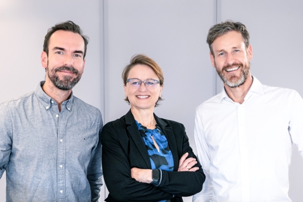 Eine Frau und zwei Männer stehen an einem Tisch und unterhalten sich. Eine Frau und zwei Männer stehen an einem Tisch und unterhalten sich.