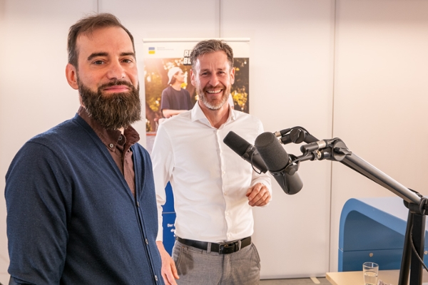 Zwei Männer stehen an einem Tisch und unterhalten sich. Zwei Männer stehen an einem Tisch und unterhalten sich.