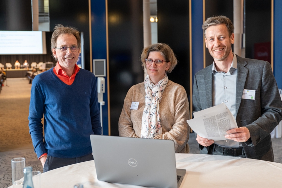 Zwei Männer und eine Frau stehen an einem runden Tisch Zwei Männer und eine Frau stehen an einem runden Tisch